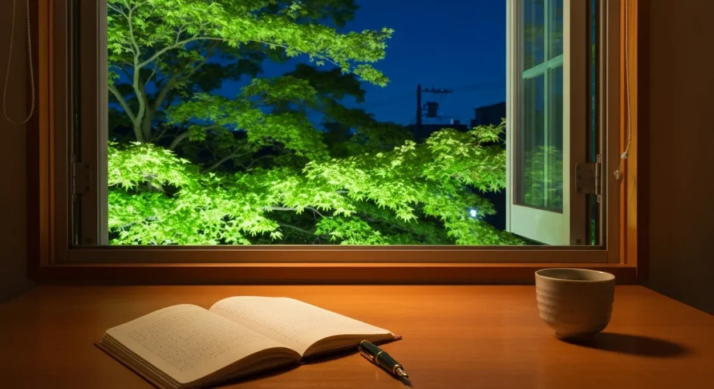 夜の窓辺に置かれた万年筆とノート、外に見える新緑の木々