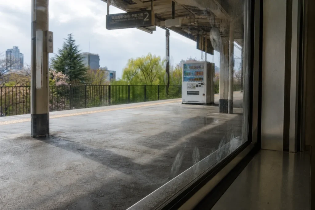 薄曇りの駅ホーム、窓の指紋が光を反射する静かな場面