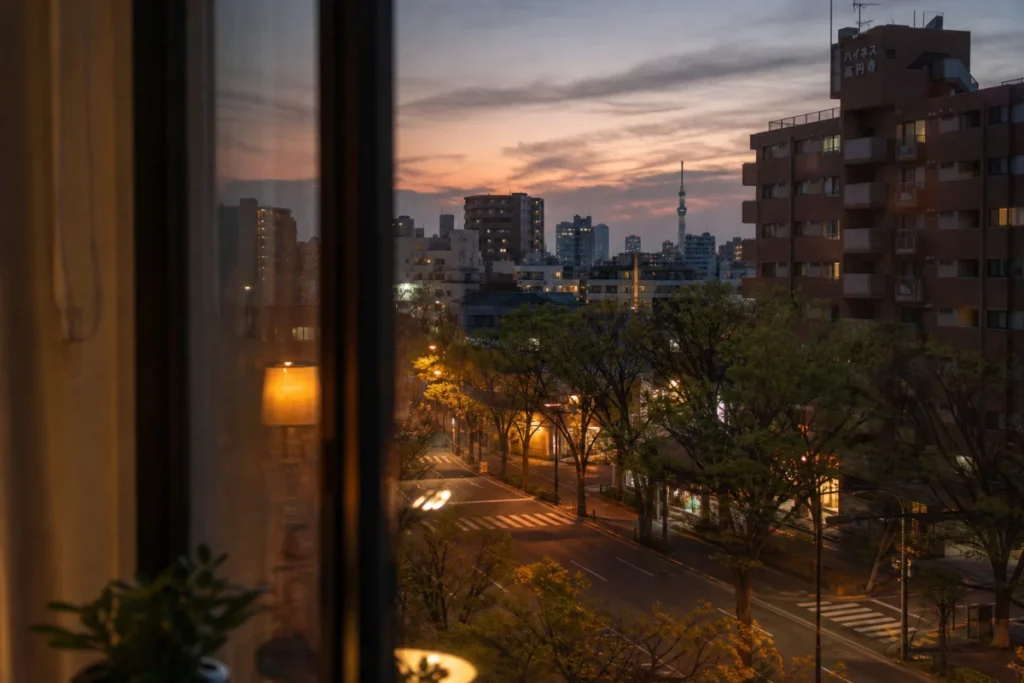 薄曇りの夕暮れ、窓越しに見える街路樹と街灯の暖かな光